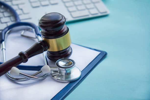 A judge's gavel resting on a stethoscope next to a keyboard and clipboard, representing medical law.