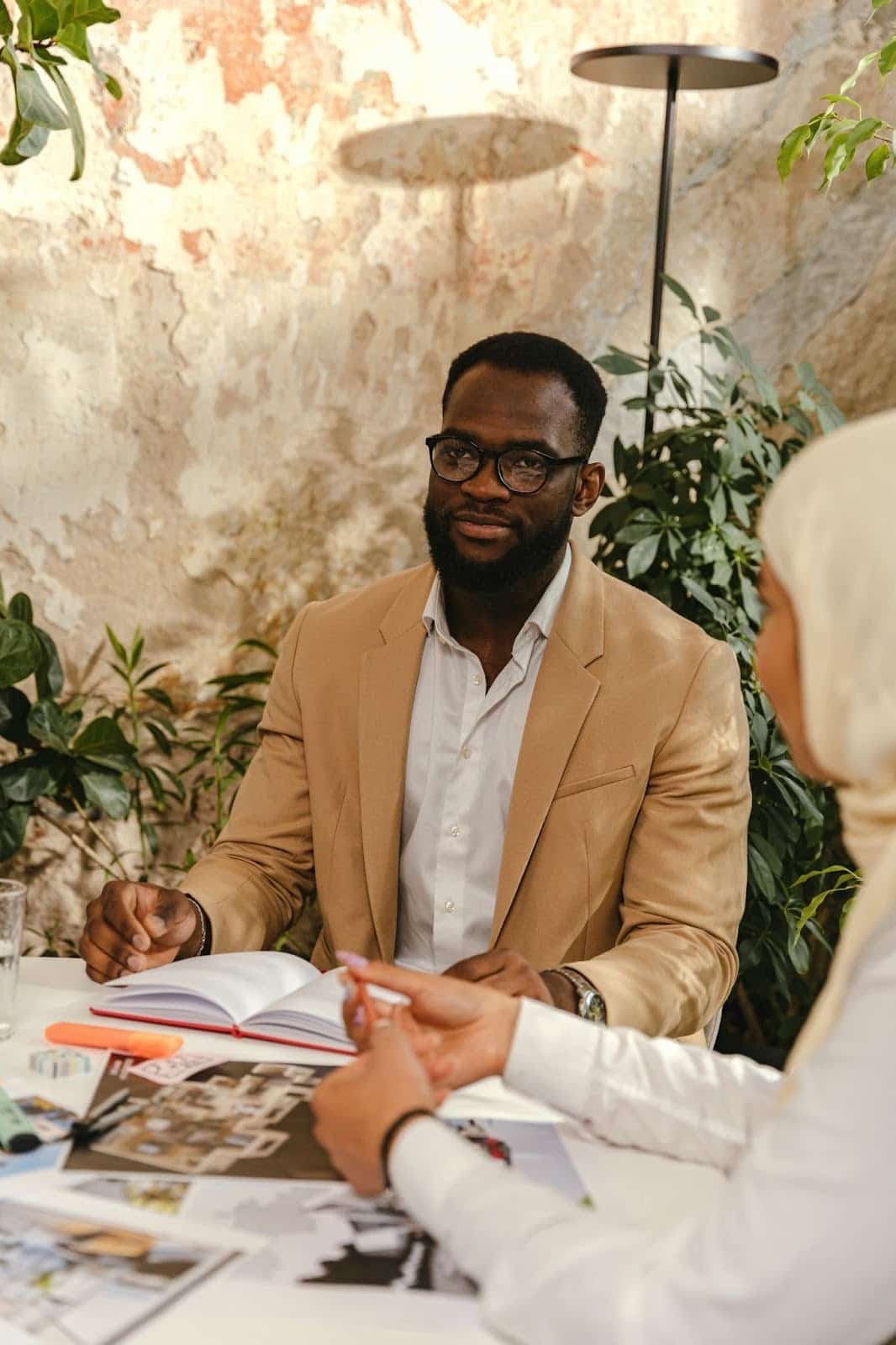 A man sitting at a table with a notebook and plans, engaged in a professional consultation with a woman