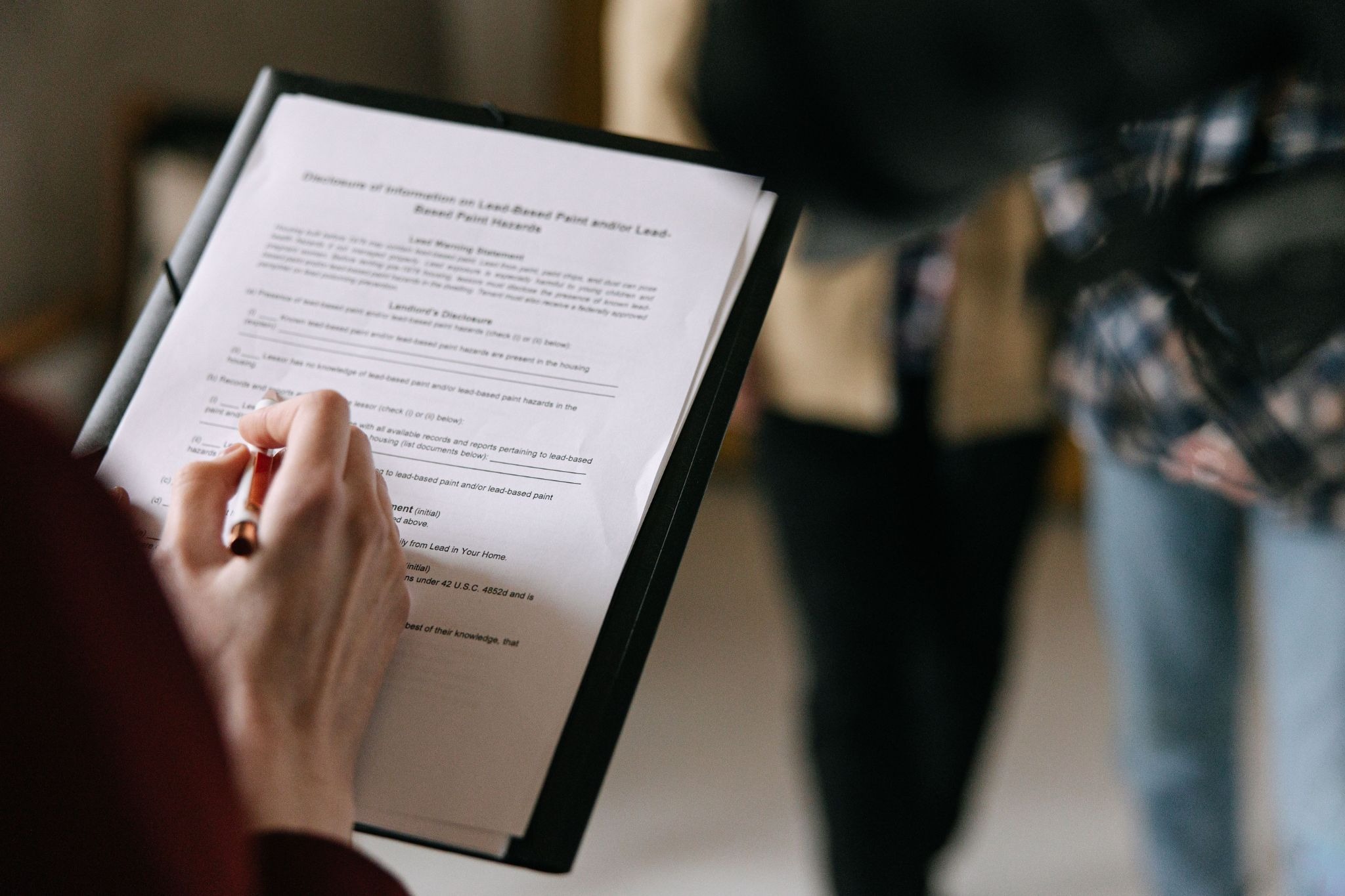 Close-up of a hand signing a paper document held on a clipboard.