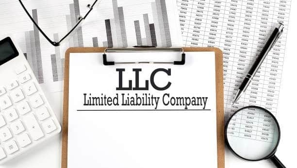 Clipboard with 'LLC - Limited Liability Company' written on paper, surrounded by a calculator, pen, magnifying glass, and financial charts.