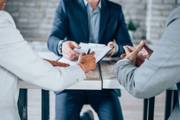 Three business professionals reviewing and signing documents at a meeting table.